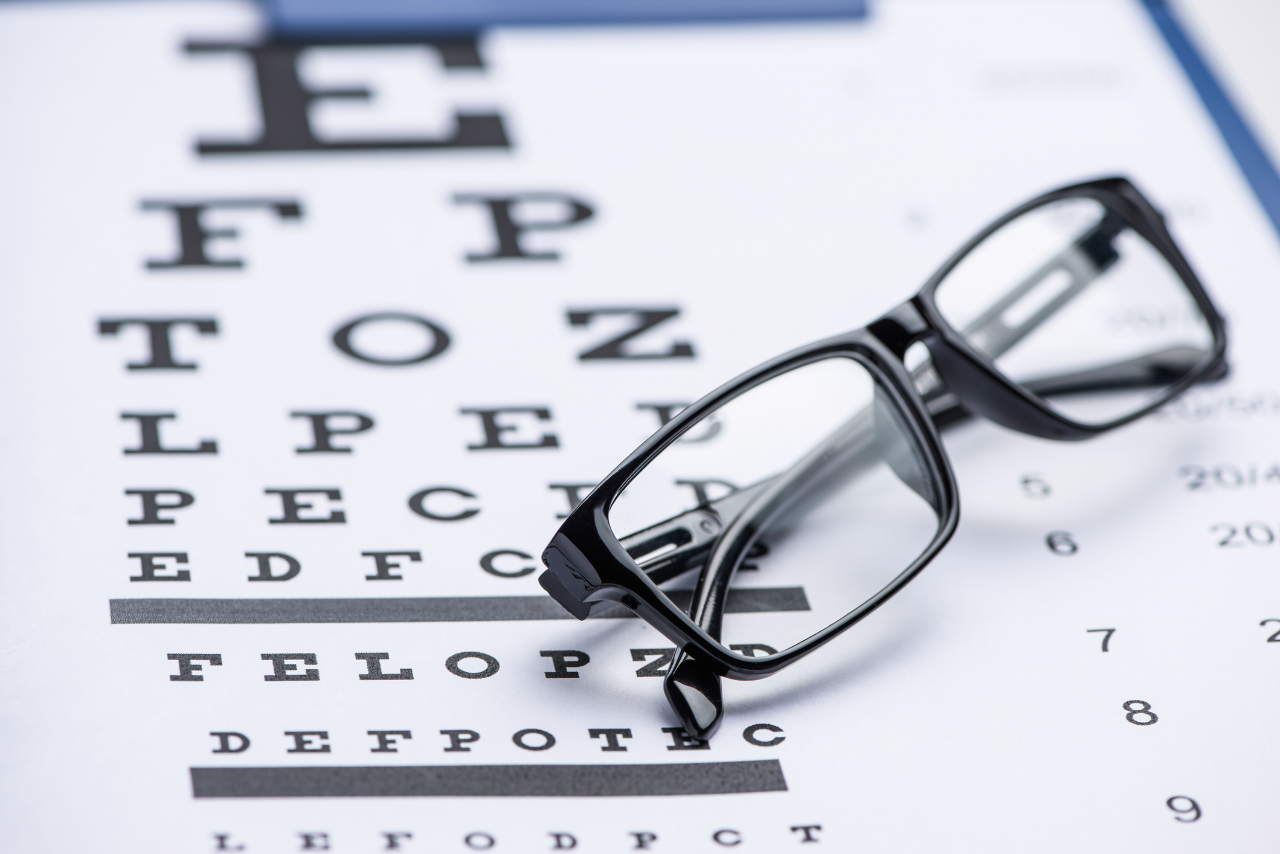 Eye test chart out of focus on white with glasses in foreground